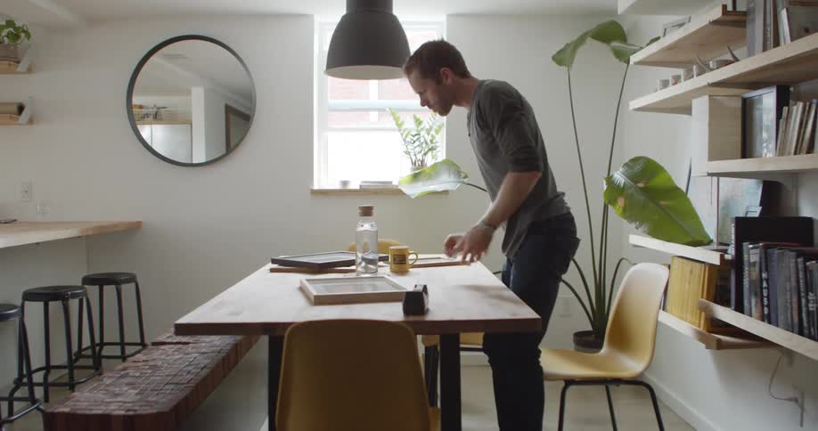 A man examines a picture frame and gets cup to drink from his coffee mug