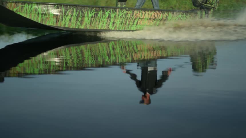 Small green and brown boat driving down a river with a man standing up inside of it