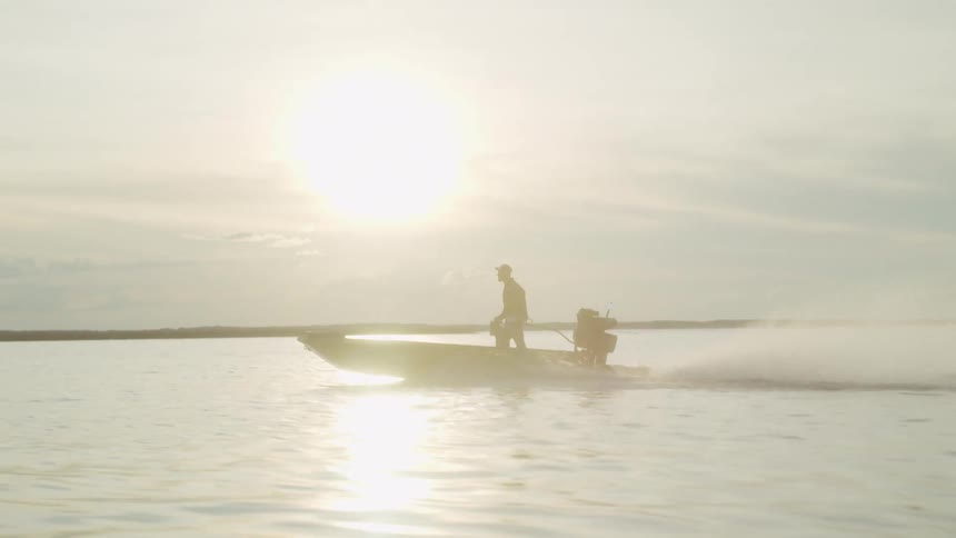 A man drives a motorboat across a lake on a cloudy day