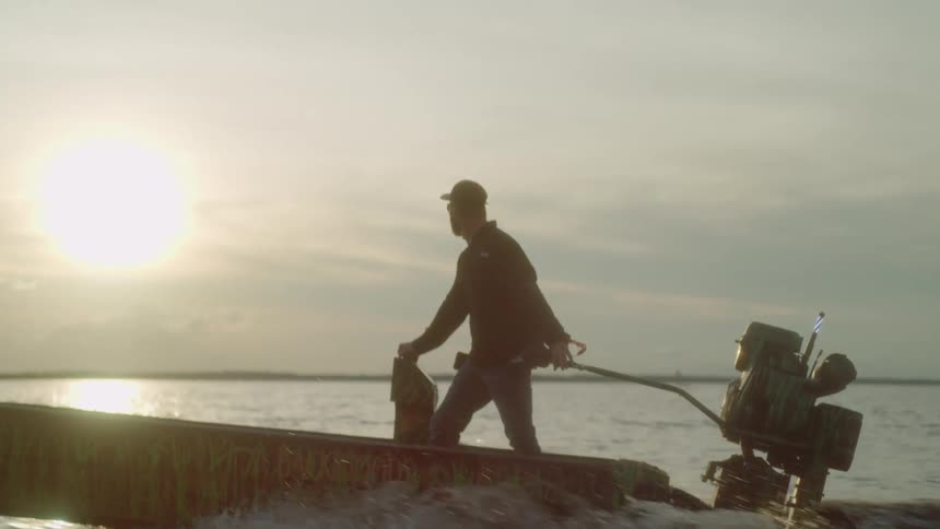 A man stands in a motorboat as he steers it across a body of water