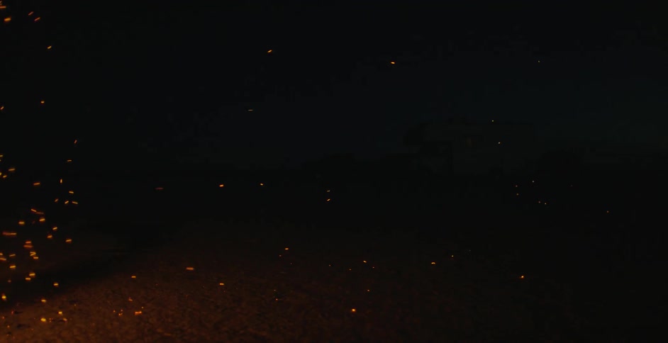 Sparks from a campfire float in a night sky