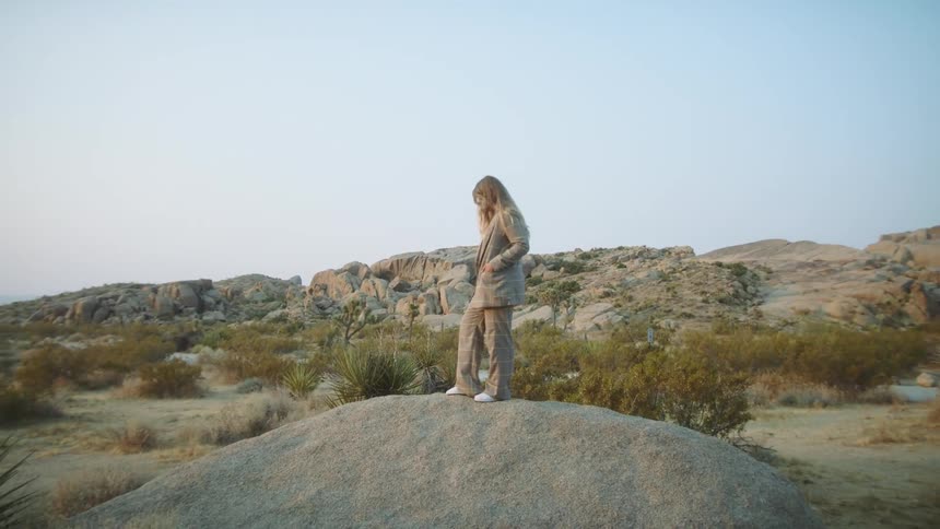 Blonde woman with a blazer and pants stands on a big rock on the plain