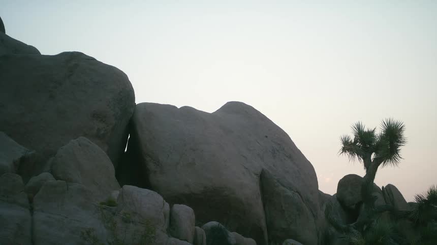 The sun is low in the sky behind some large boulders located on a slope