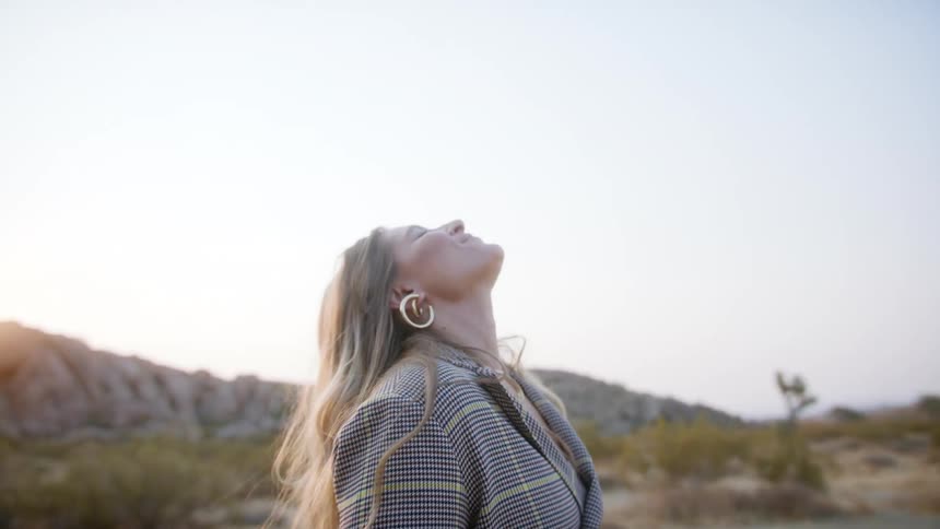 A woman with long blonde hair stands outside in the desert