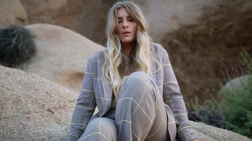 A plus size model poses on a large boulder outside in a glen plaid suit