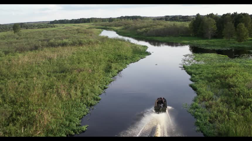 A motorboat leaves a wake as it travels on a curving narrow body of water