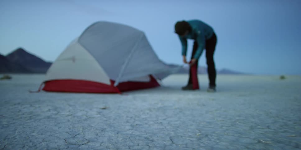 A man is setting up a tent on a sunny day