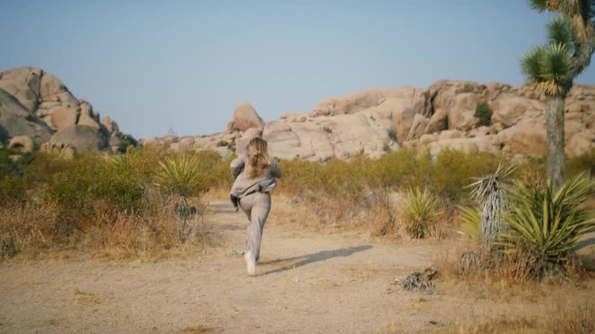 A woman in a plaid suit and sneakers runs through a desert canyon