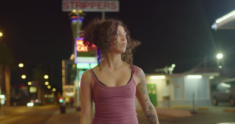 A woman walks a city sidewalk by herself at night
