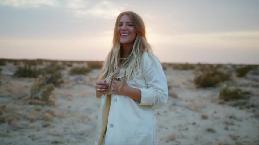 A middle aged caucasian woman dressed entirely in white dances in the sands of a desert in the evening