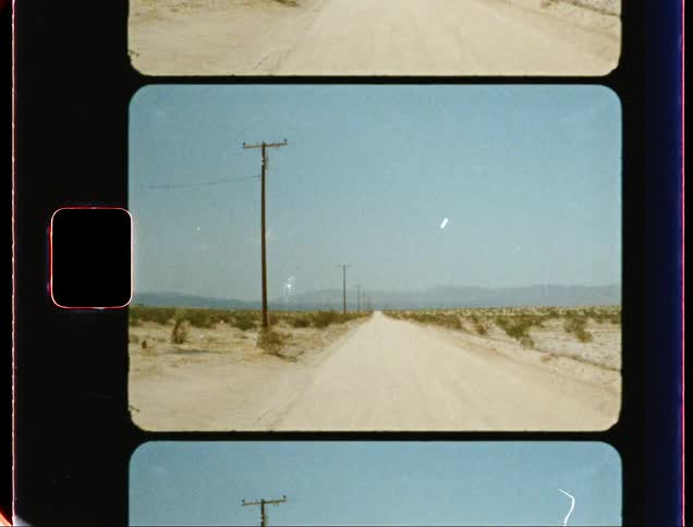A row of telephone poles line an abandoned and dusty desert road
