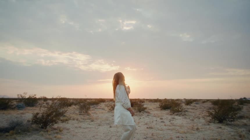 A blonde woman dances around by herself in a desert area