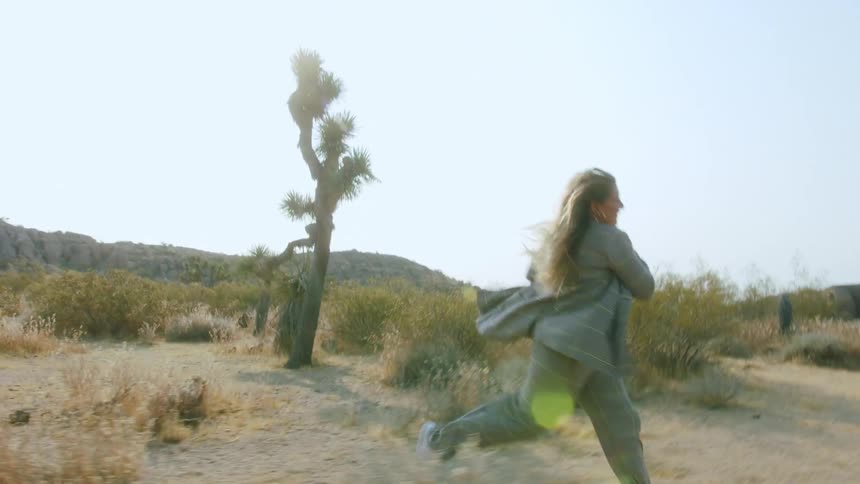 Blonde female running with white shoes wearing a shirt and pants and white tennis shoes running through a desert setting