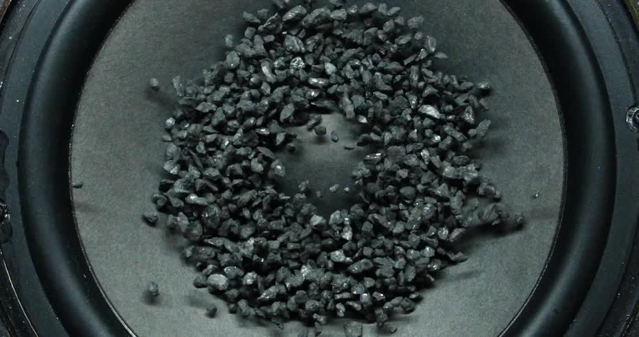 Several coarse gray pebbles bounce around on a vibrating audio speaker