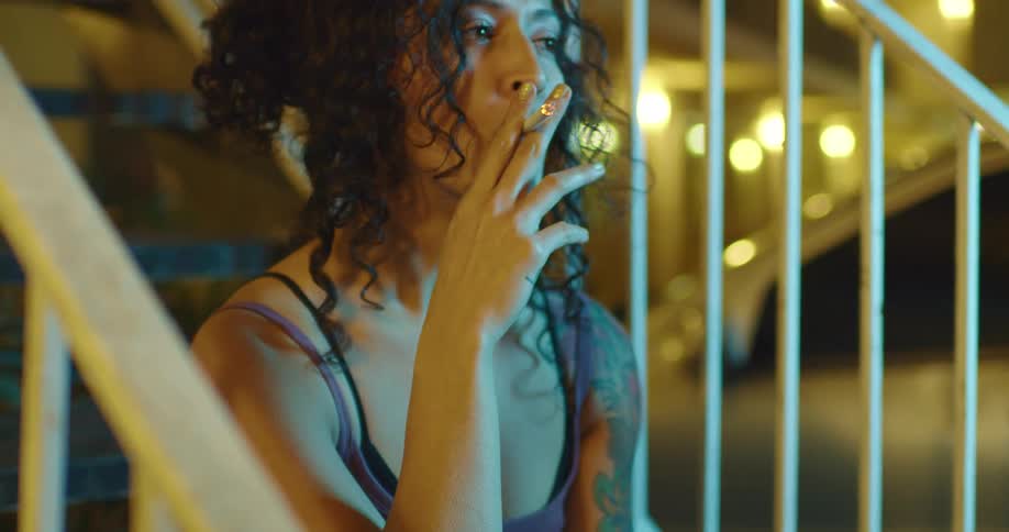 Woman sitting on a stair case at night smoking a cigarette
