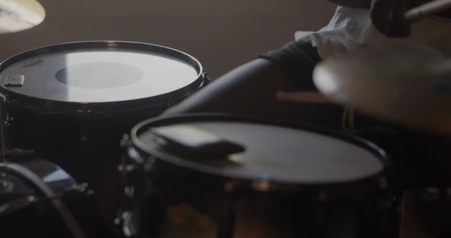 Male drummer with black shorts and a white shirt plays the drums in a room
