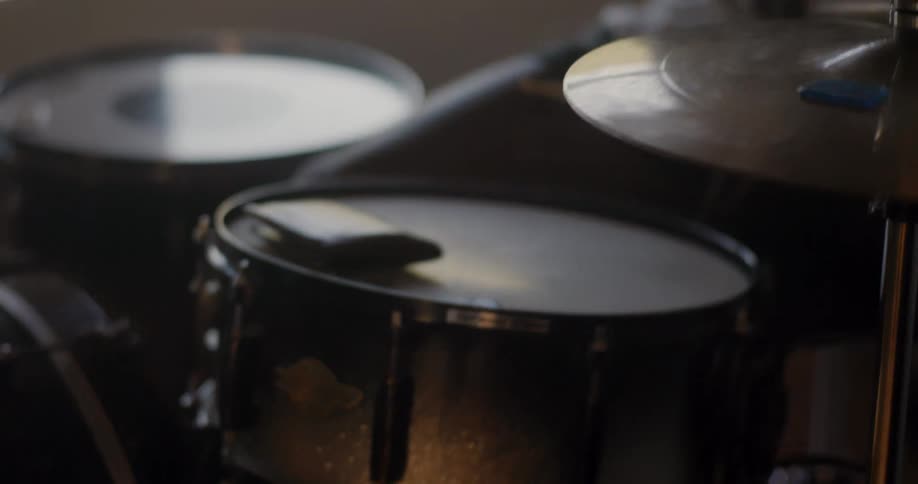 A man is practicing the drums in a small room with a window