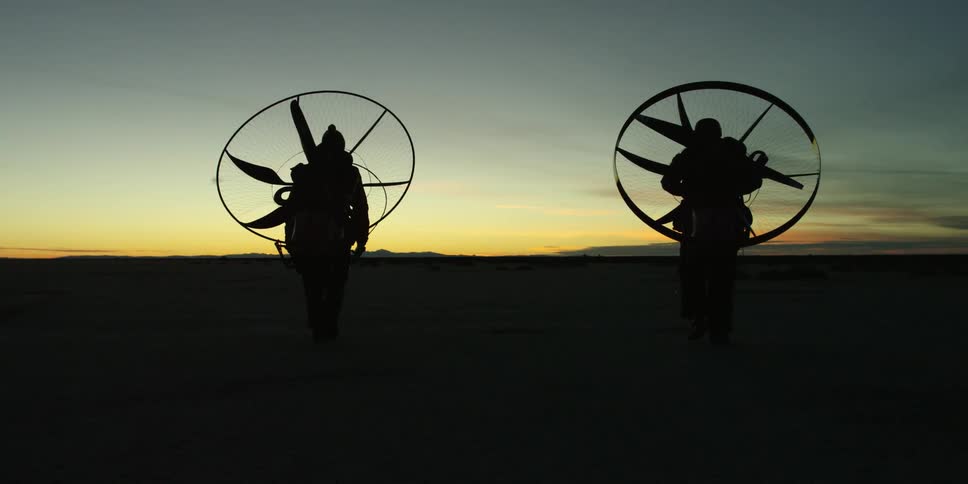 People wearing paramotors on their back as they walk across a plain