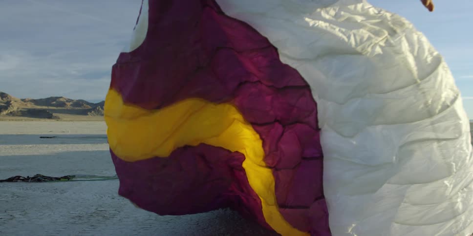 A person stretches a purple, gold, and white parachute on the ground