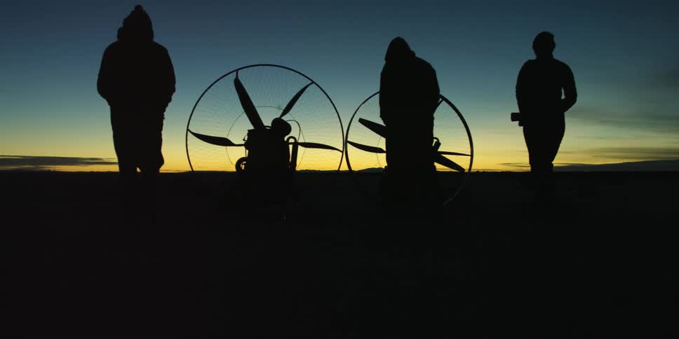 Three people walk toward motorized hang gliders at dusk