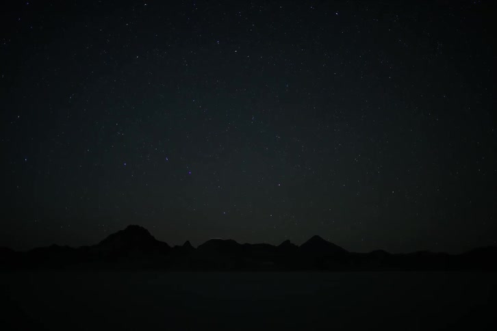 A shooting star crosses the sky over a mountain