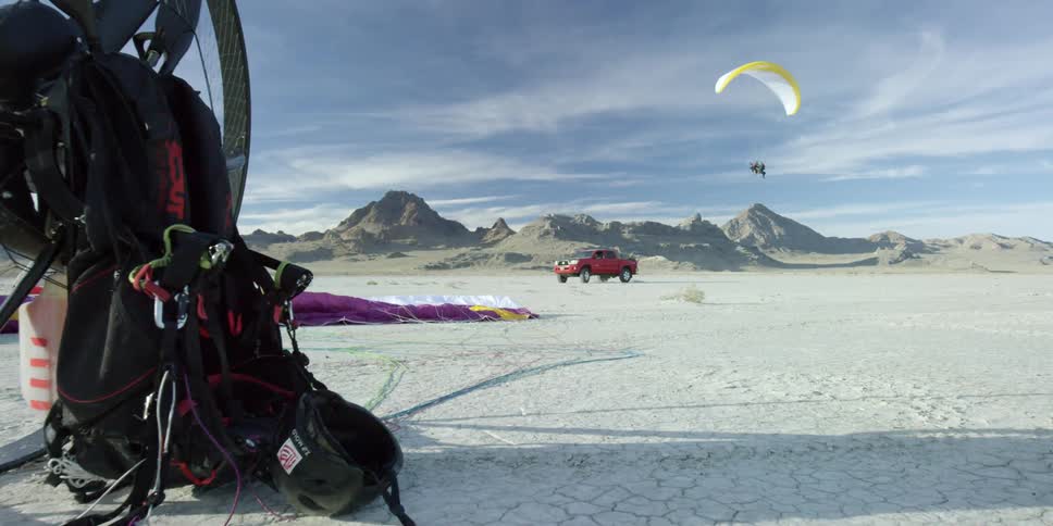 Red pickup driving on a plain with someone paragliding above them