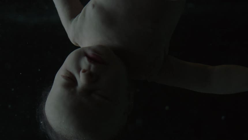 Baby floats upside down in fluid against dark