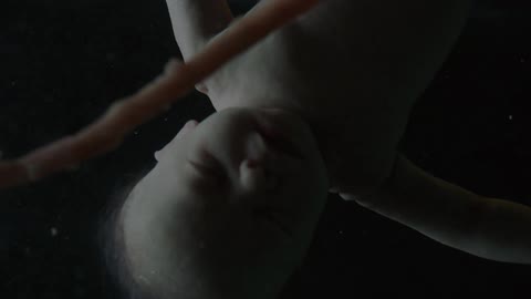 A baby floats upside down in liquid with a cord showing with strobes of light and then darkness