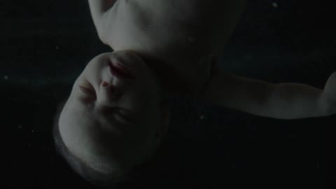 A baby with white skin floats with a black background