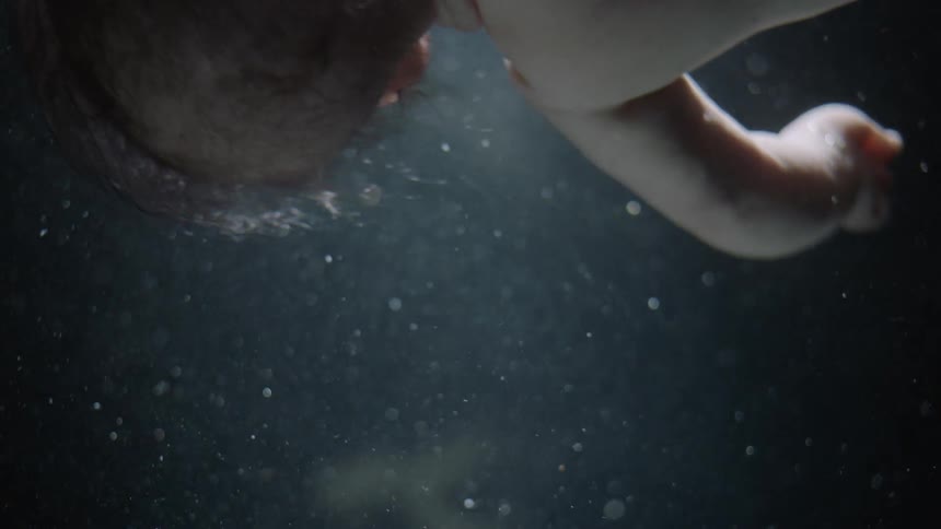 An infant is floating in a fluid in a dark room lit by a single spotlight