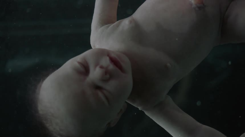 A baby with umbilical cord attached floats and turns in liquid