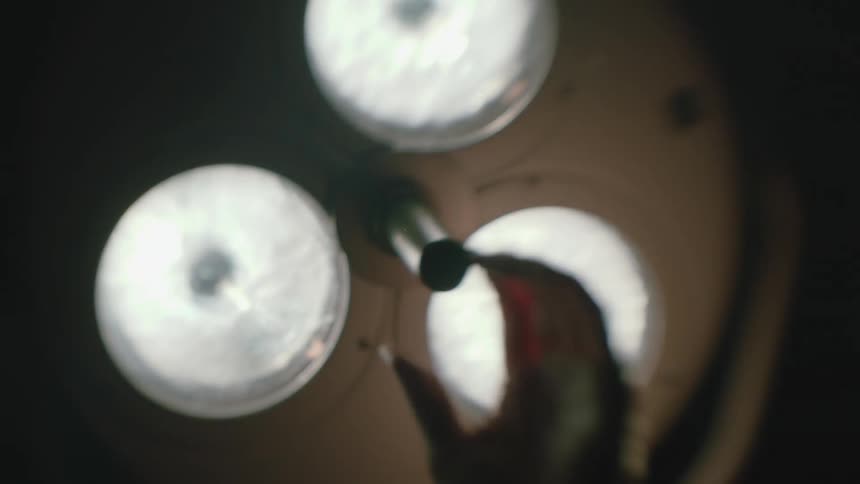 An operating room light with three lights being adjusted by a hand reaching up and the lights go out