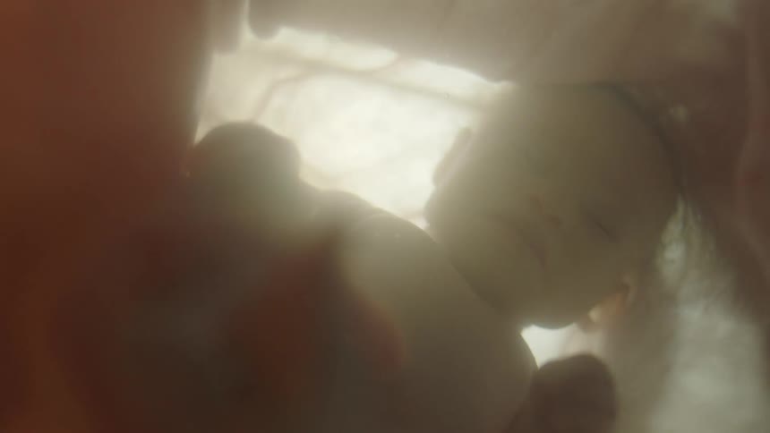 A baby floating in liquid with gauzy layers surround it and flashes of light