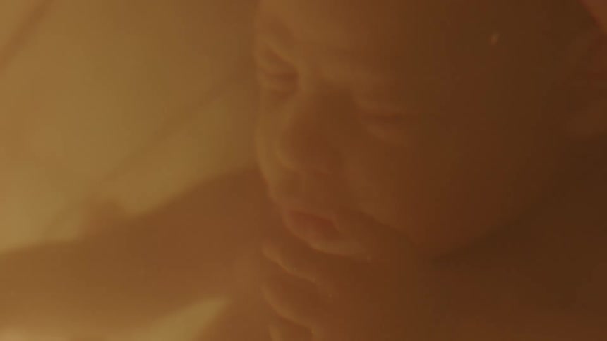 Unborn baby floats in cloudy liquid as condensation runs down side