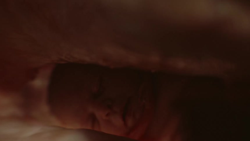 A blanket is lifted to reveal an infant fast asleep