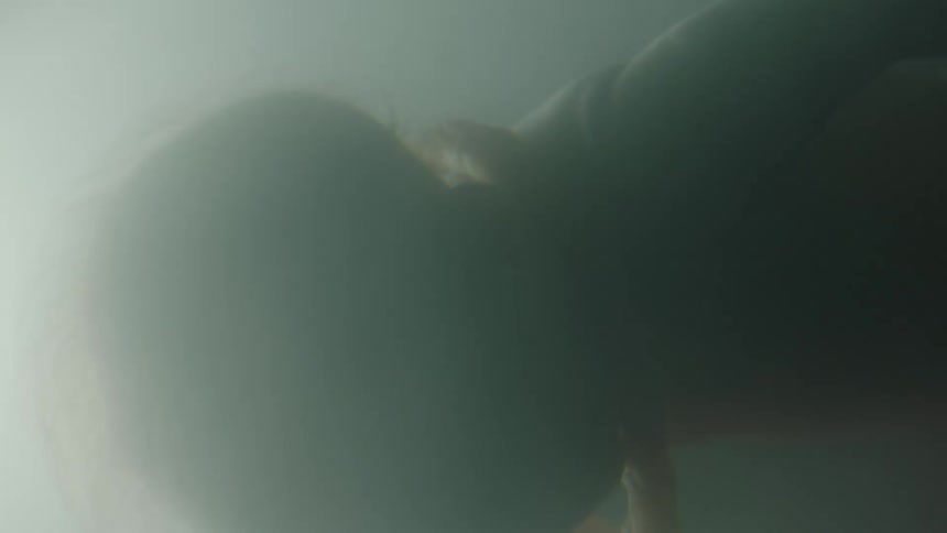 A baby floats in liquid with shades of gray and vague light