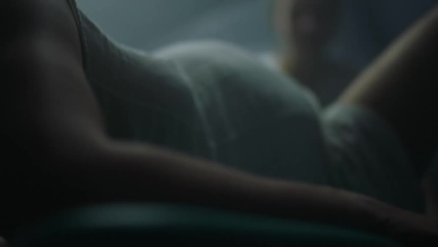 A woman is in labor on a hospital bed surrounded by medical staff with one hand grasping the side of the bed