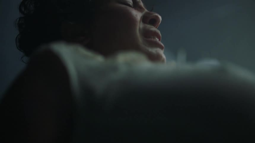 Pregnant woman feels pain while pushing giving birth on a dimly lit hospital room