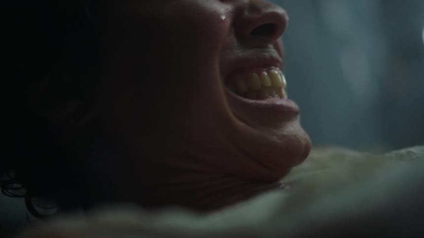 A woman in labor grimaces in pain while laying on a hospital bed
