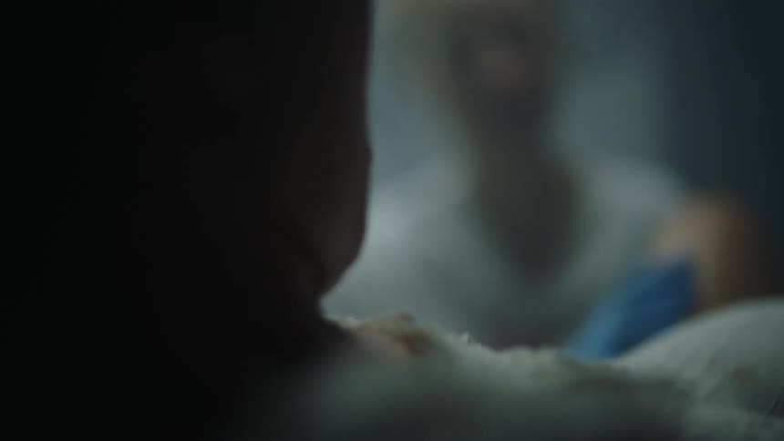 A woman is lying on a bed in labor in a hospital sweating wearing a white nightgown