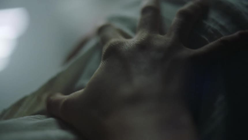 A hand clutches a pregnant stomach as the woman is lying on her back