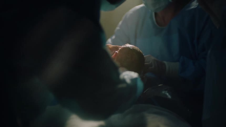 Surgeons removing a baby being delivered via caesarean delivery in a hospital room