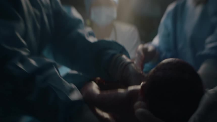 A physician holds up a newborn baby and places it onto a blanket