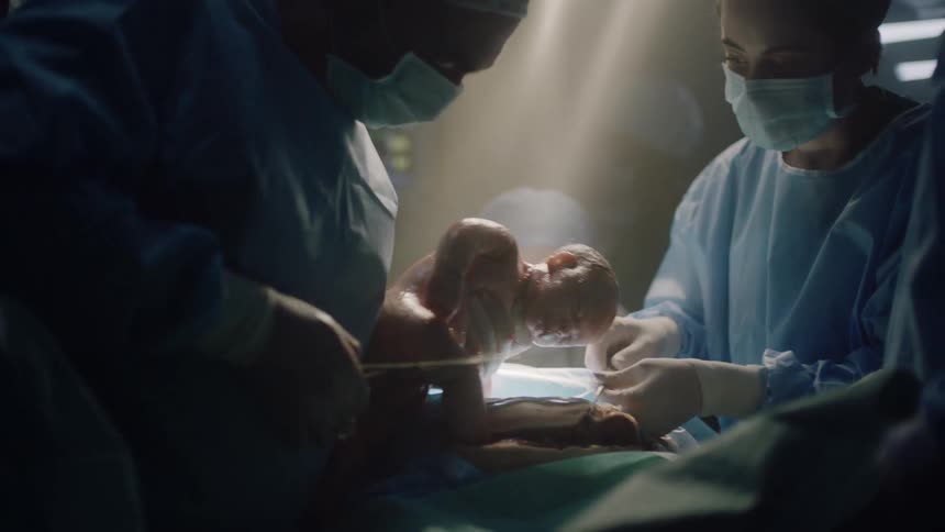 Baby is being born via c section with medical staff completing the procedure