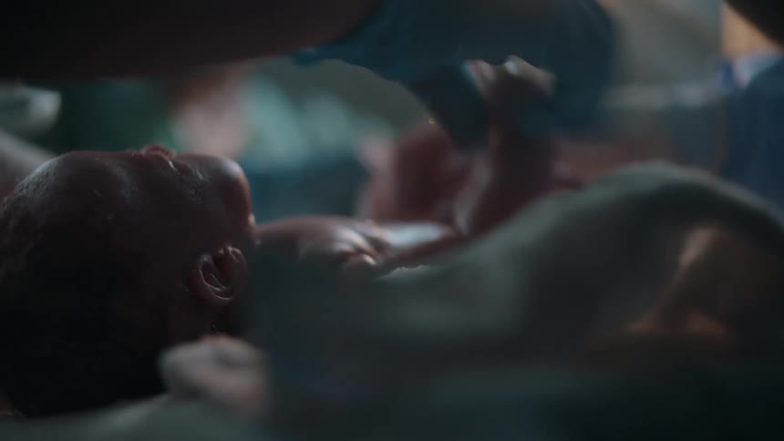 A newborn is being assessed by medical staff just after birth in an operating room