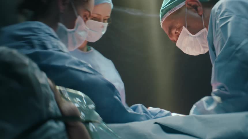 A doctor delivers a baby by cesarean and hands him off to a nurse before cutting the cord