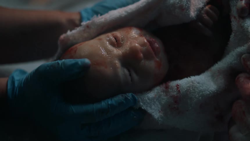 A newly born baby is wrapped in a cloth and caressed by someone with gloved hands