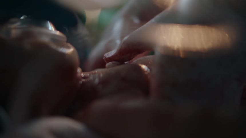 A doctor uses their thumbs to perform cpr on a bloody newborn baby wearing an oxygen mask in a hospital