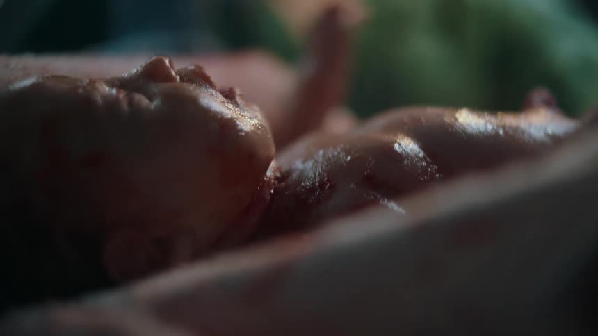 Newborn human baby attended by doctors on a dimly lit hospital