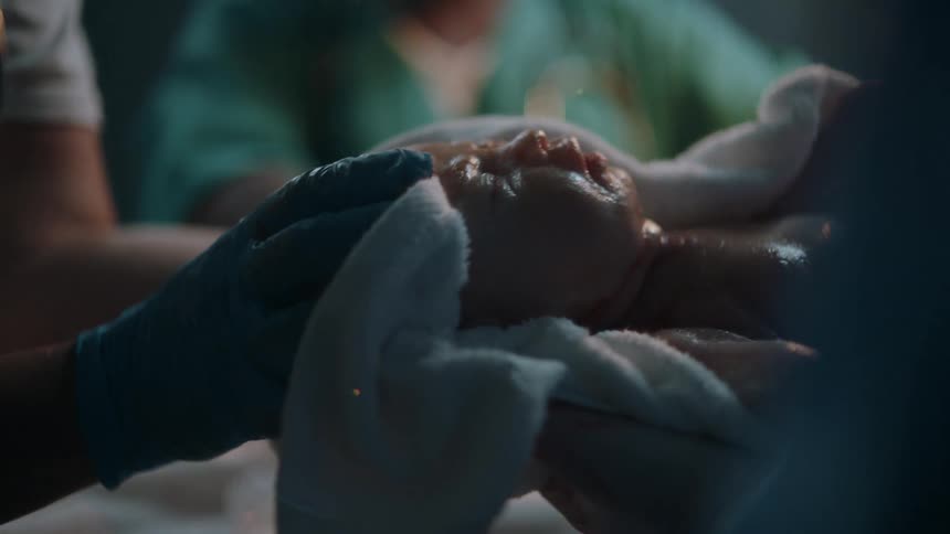 A medical person holds a baby to be swaddled with a blanket after birth in a hospital